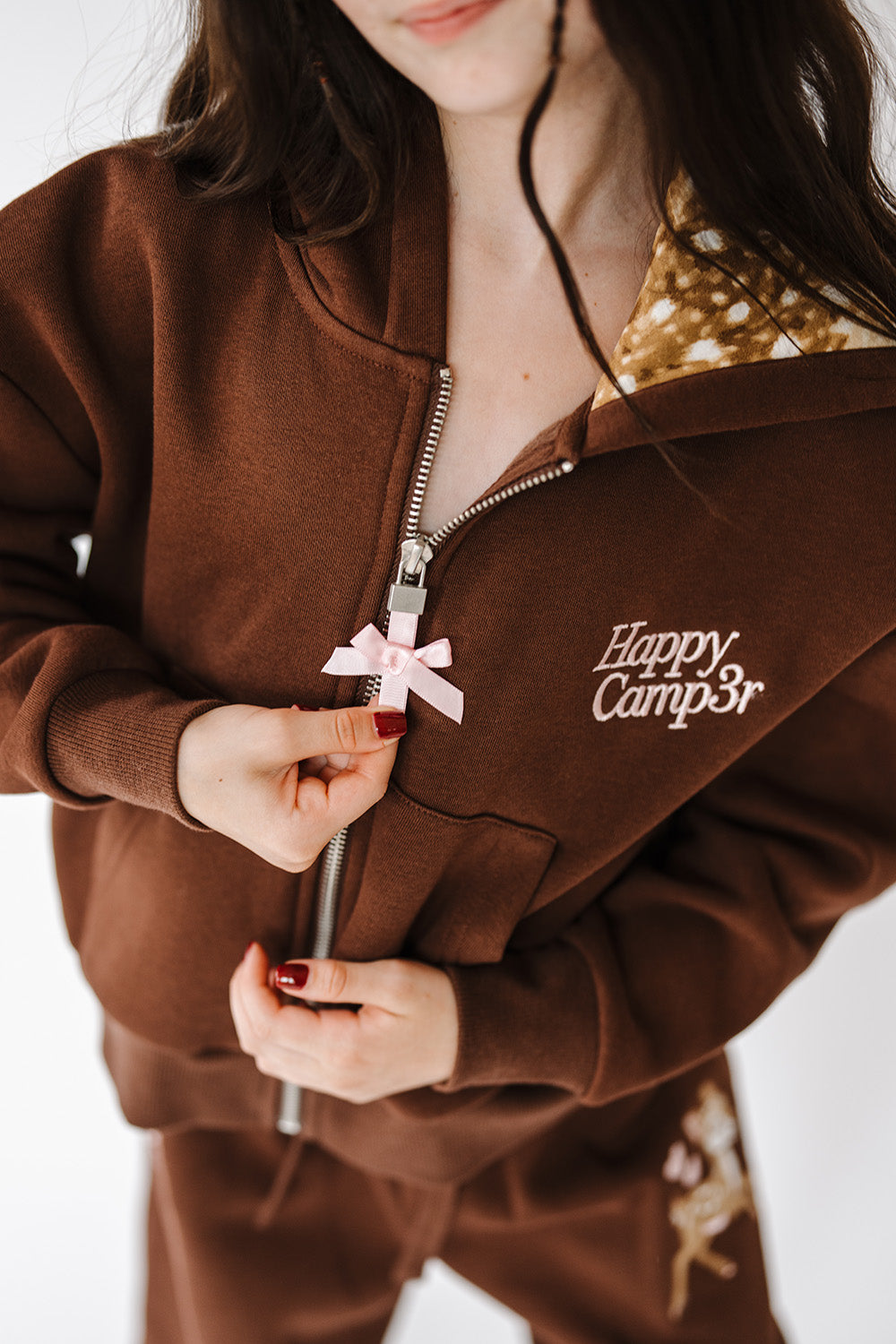 Close up of the bow zipper pull and logo on the Fawn Love Youth Zip Up Hoodie. The Happy Camp3r
