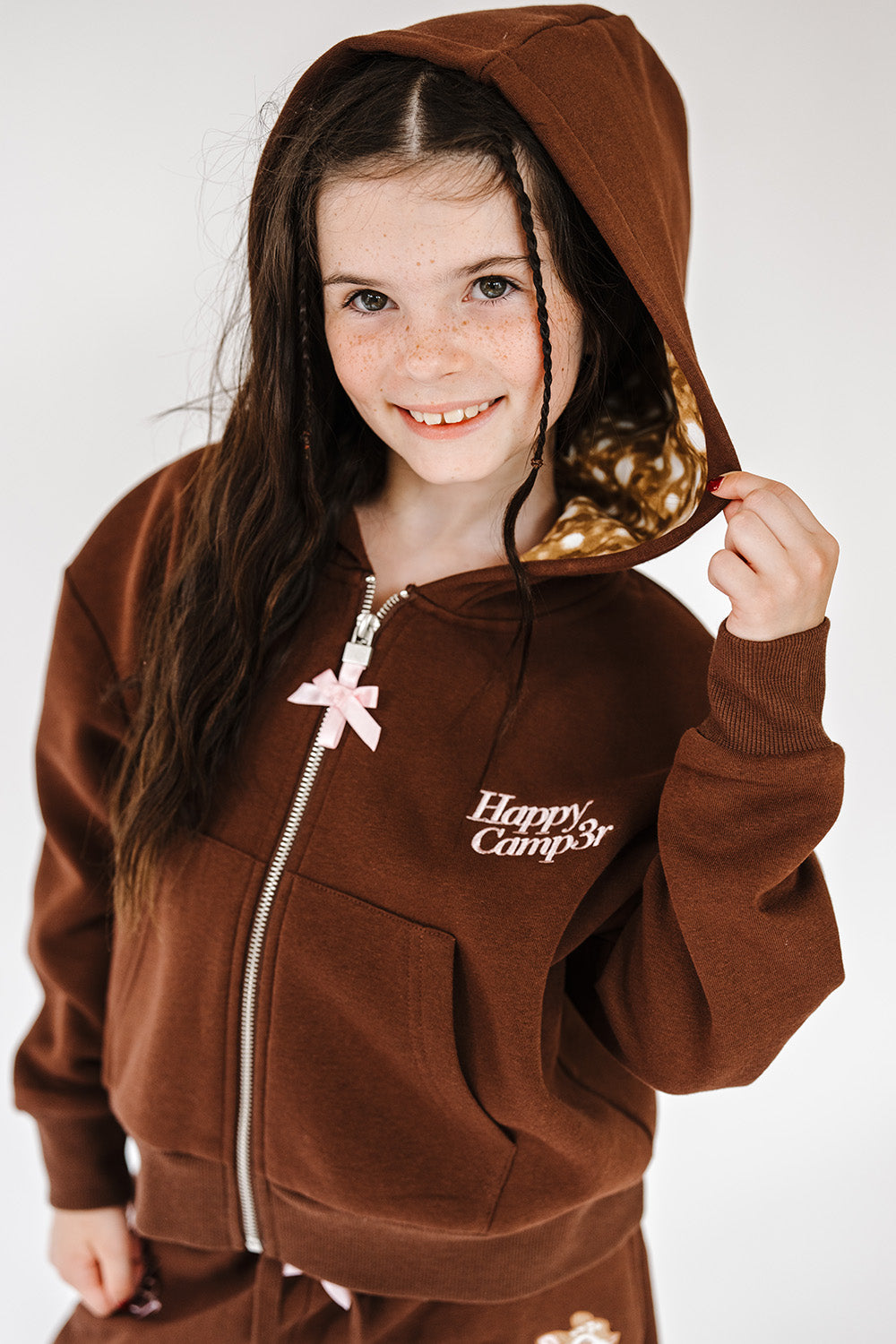Girl in the brown Fawn Love Youth Zip Up Hoodie with fawn print lined hood, front view. The Happy Camp3r