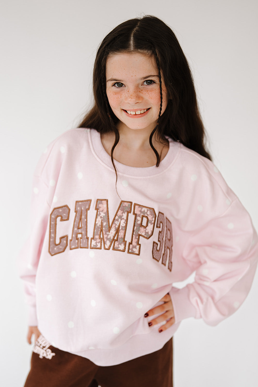 Girl in the Pink Sprinkle Camp3r Youth Crewneck with Camp3r varsity lettering, front view. The Happy Camp3r