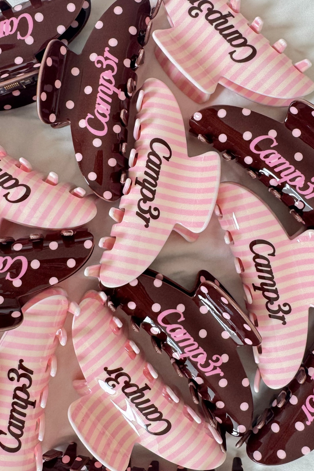 Pile of pink striped and brown polka dot claw hair clips with Camp3r script. The Happy Camp3r