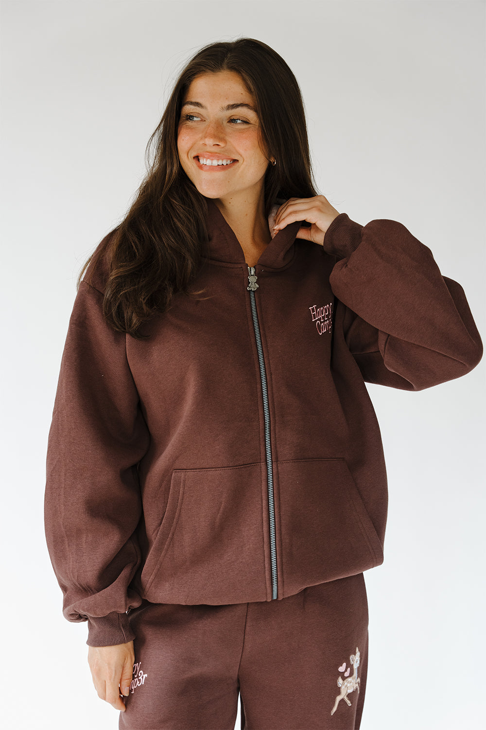 Model in the brown Fawn Love Zip Up Hoodie with small chest logo, front view. The Happy Camp3r